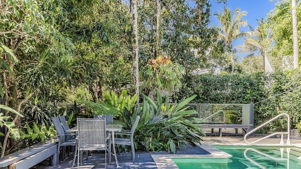 A pool area with lounge chairs and a table surrounded by lush greenery. - Dreamtime Dune Studio (Fingal Head)
