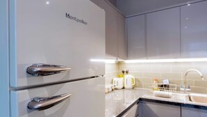 Een moderne keuken met een witte koelkast, roestvrijstalen handgrepen en een aanrecht met waterkoker en broodrooster.