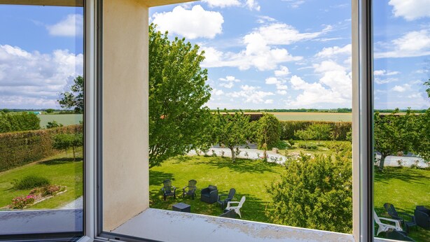 A view from a window overlooking a well-maintained garden with outdoor seating and a clear sky.