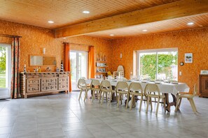 A dining area with a long table, chairs, a wooden cabinet, and a window with a view of greenery. - Gite Phare - Moulin du Cher: Tranquility Near La Rochelle and the Coast (Chambon)
