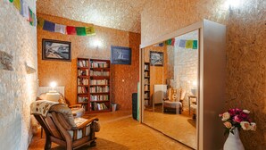 A cozy room with a wooden floor, a wooden chair, a bookshelf, and a mirror reflecting another room.