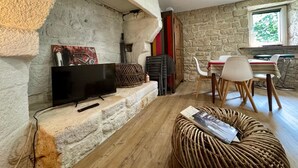 Ein gemütlicher Wohnbereich mit Steinwand, Flachbildfernseher, Rattan-Pouff und Esstisch mit Stühlen.