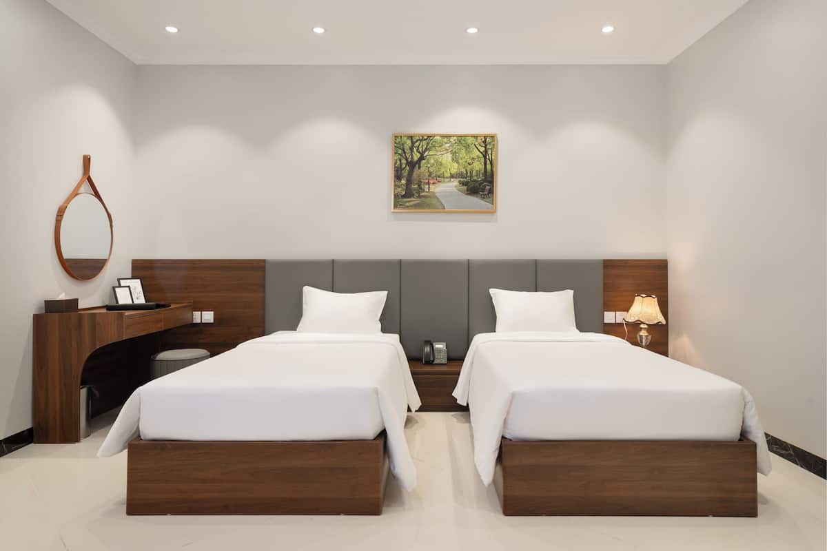 Une chambre d’hôtel moderne avec deux lits, un bureau, un miroir, un tableau et une lampe.