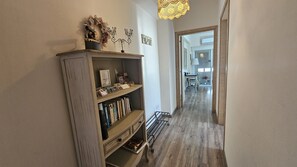 A hallway with a wooden bookshelf, a chandelier, and a dining area in the background. - 116 NIC 303 - Stay Vintage Central Suites (Nicosia)
