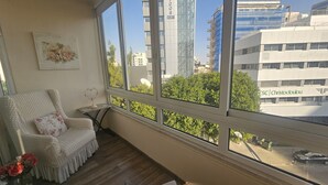A room with a large window overlooking a cityscape, including a building with 'TOWER' signage and another with 'ESC | Christodoulou' branding. - 116 NIC 303 - Stay Vintage Central Suites (Nicosia)