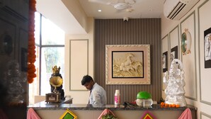 A reception area with a counter, a ceiling fan, a framed artwork, and a statue. - Prince Diamond Boutique Hotel (Varanasi)