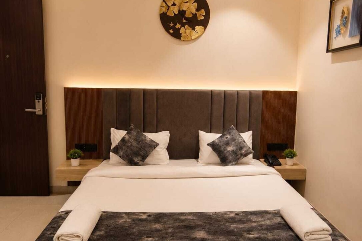 A modern hotel room with a large bed, a headboard with vertical slats, a round wall decoration, and a small bedside table with a plant.