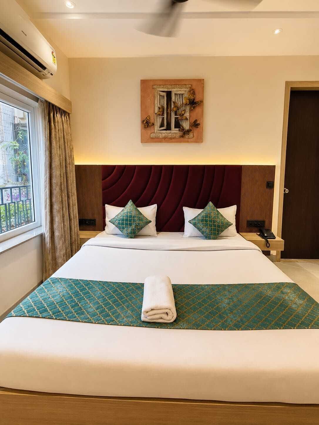 Ein Hotelzimmer mit einem großen Bett, einem Deckenventilator, einem Gemälde über dem Bett und einem mit Vorhängen versehenen Fenster.