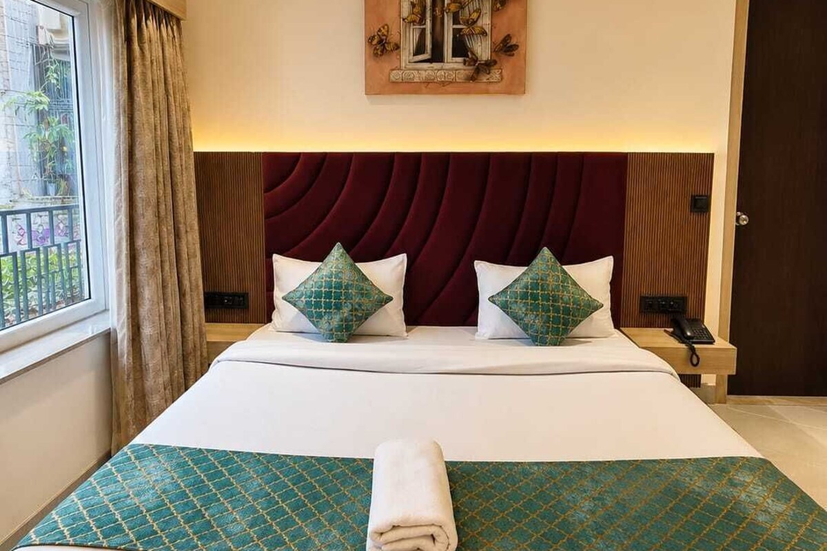 A hotel room with a large bed, a ceiling fan, a painting above the bed, and a window with curtains.
