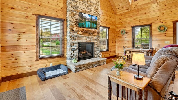A cozy cabin interior with a stone fireplace, wooden walls, a sofa, and a dining table. - Valley View Cabin at Trickle Creek (Logan)