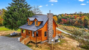 A log cabin with a stone chimney, a porch, and a view of a forest. - Valley View Cabin at Trickle Creek (Logan)