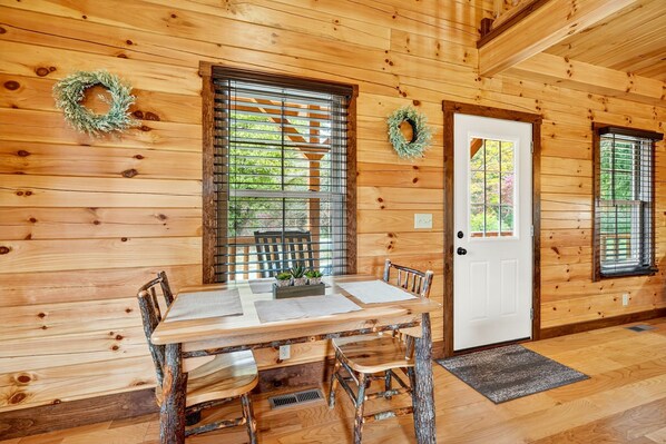A wooden interior with a dining table, chairs, a white door, and two windows with shutters. - Valley View Cabin at Trickle Creek (Logan)