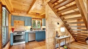 A wooden cabin interior with a kitchen, a dining area, and a staircase. - Valley View Cabin at Trickle Creek (Logan)