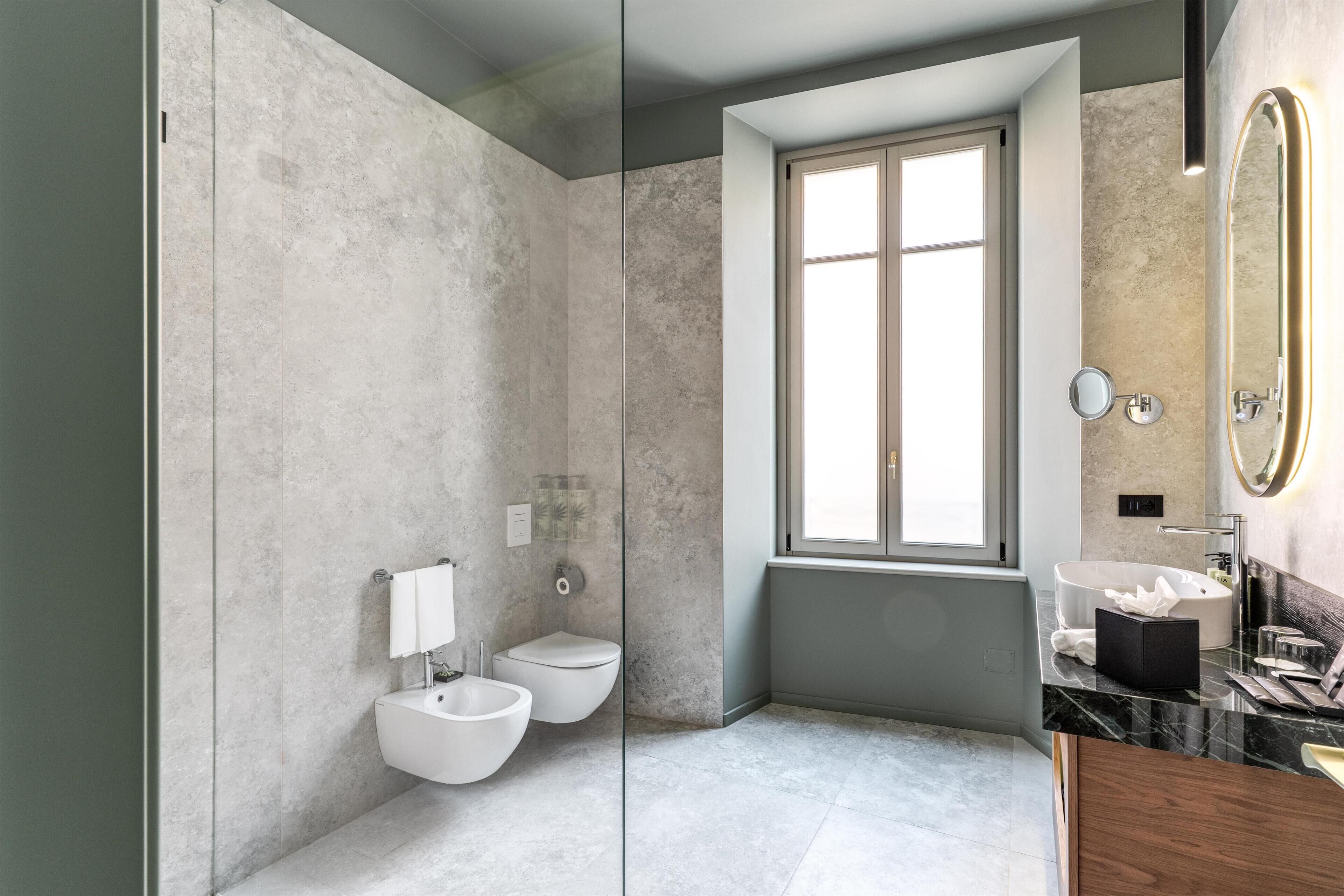 Une salle de bain moderne dotée d’une douche à parois de verre, d’un bidet, de toilettes, d’un lavabo avec un plan de travail en marbre et d’un grand miroir avec un cadre doré.