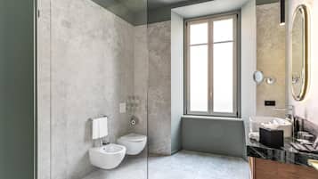 A modern bathroom with a glass shower enclosure, a bidet, a toilet, a sink with a marble countertop, and a large mirror with a gold frame.