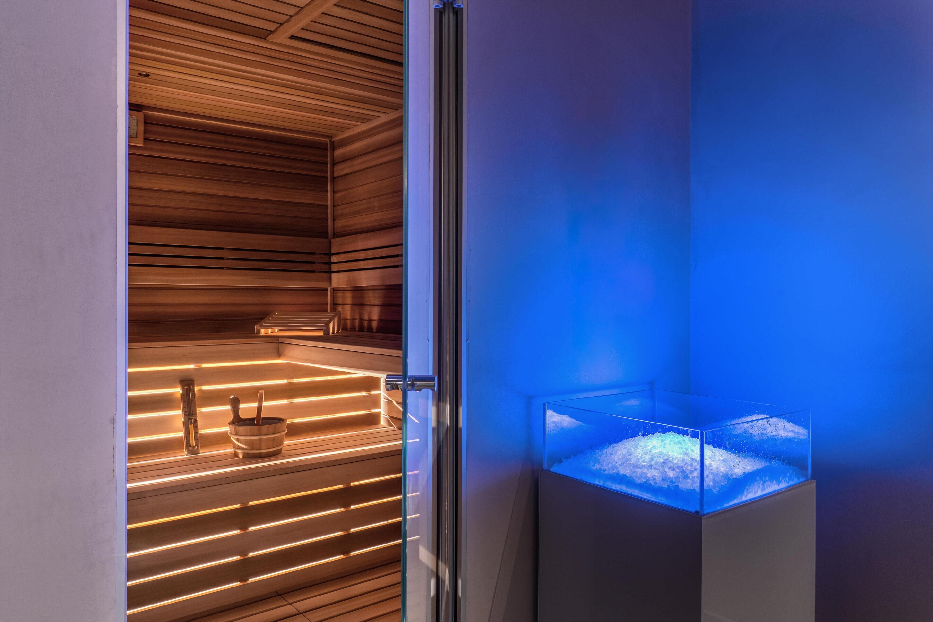 Una sauna moderna con listones de madera y cerramiento de vidrio con luz azul.