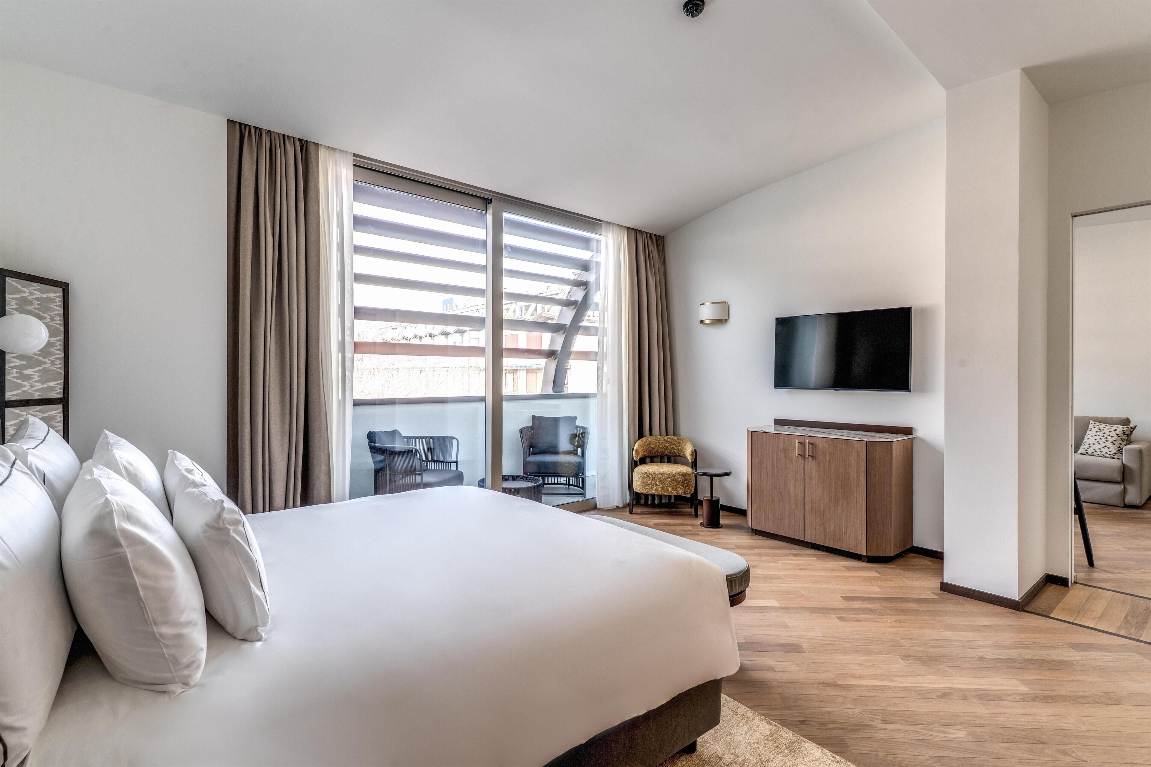 Une chambre d’hôtel moderne, dotée d’un grand lit, d’une télévision, d’un bureau et offrant une vue sur la ville.