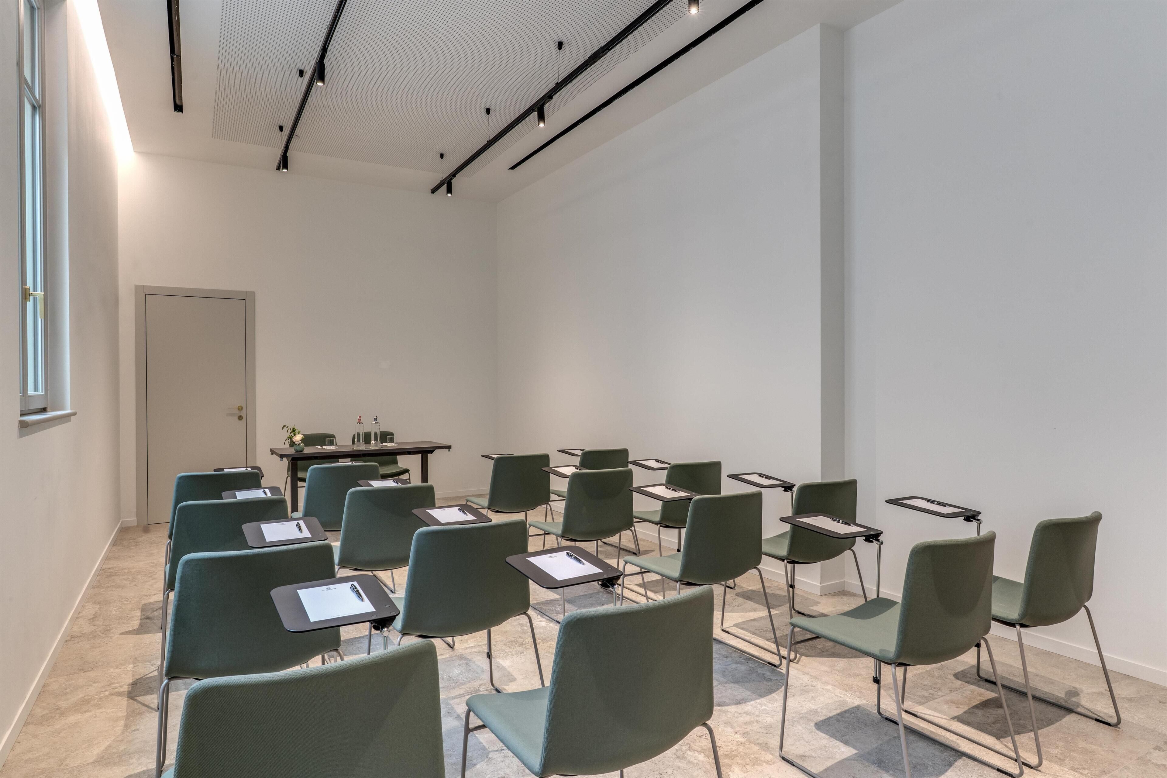 Un salón de conferencias con sillas verdes, una pizarra y una mesa con una computadora portátil.
