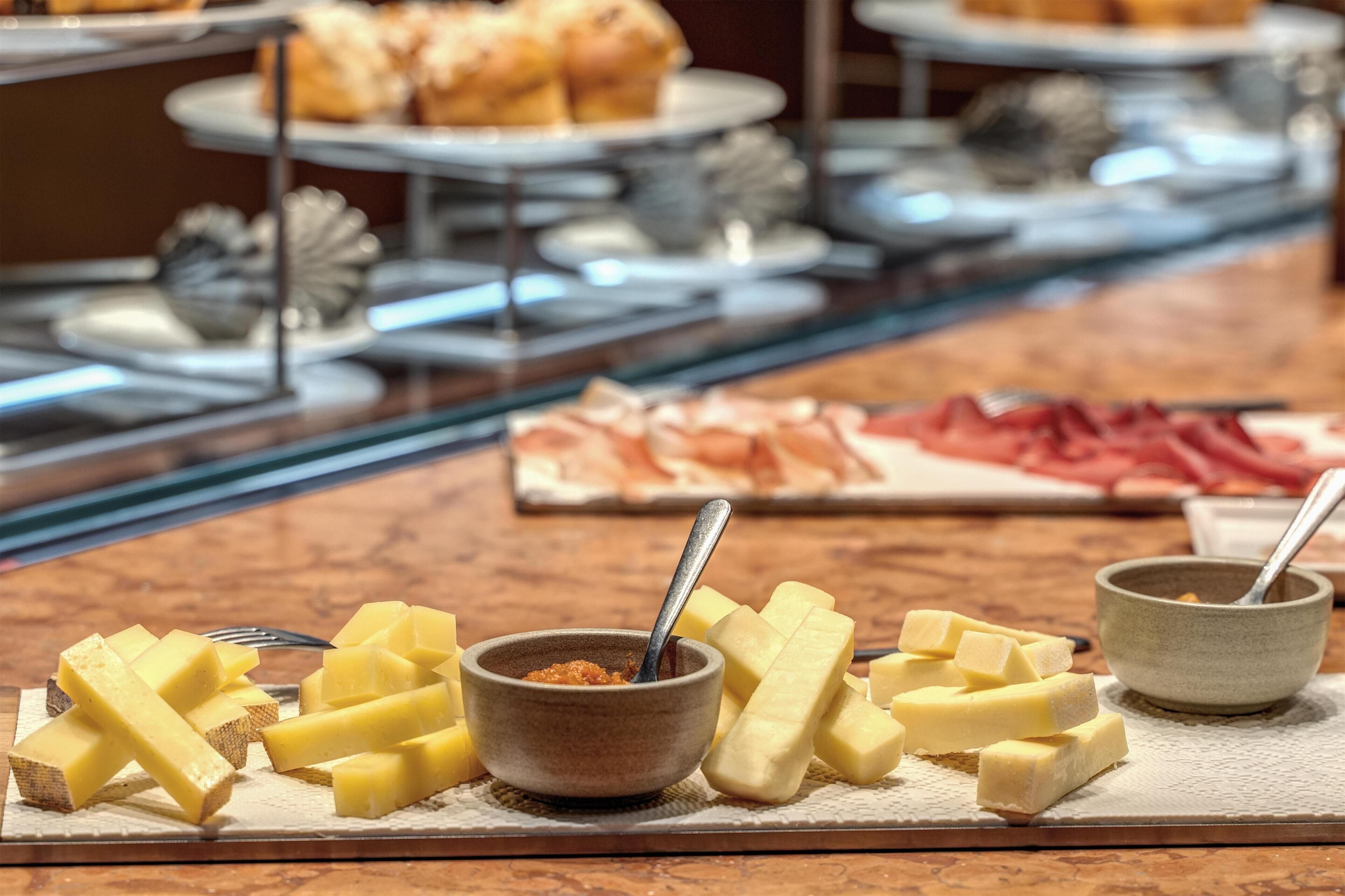 A buffet with various cheeses and meats, a bowl of sauce, and a spoon.
