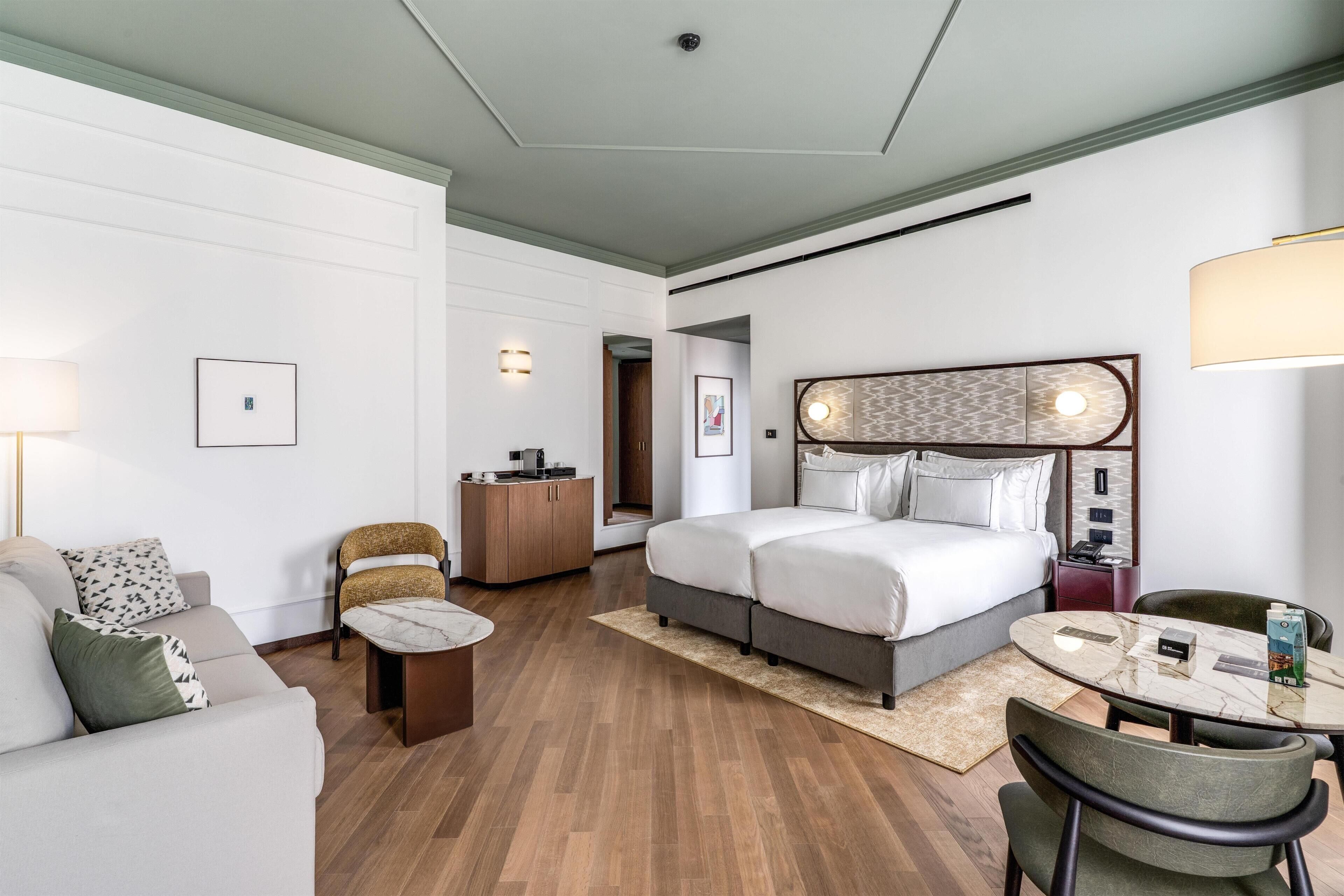 A hotel room with a bed, a desk, a chair, a sofa, and a table.
