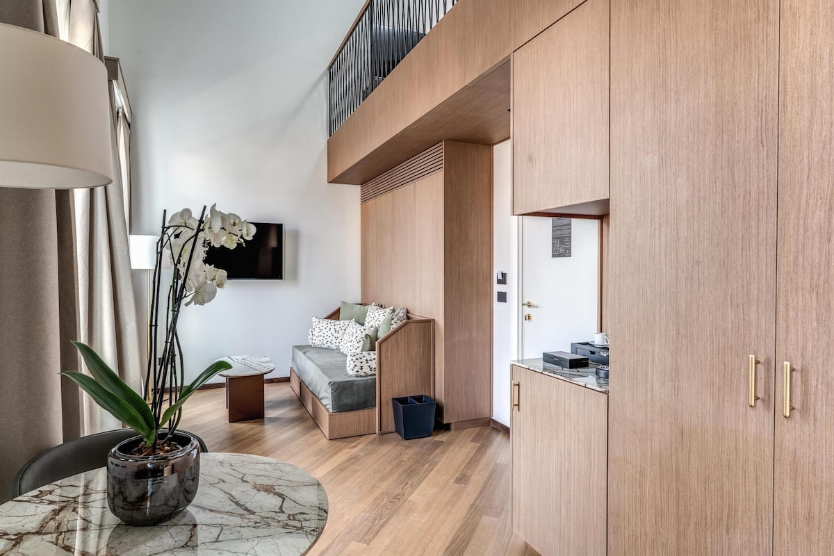 A modern room with a bed, a small table with a plant, a TV mounted on the wall, and wooden cabinets.