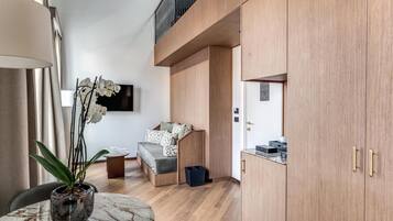 Une chambre moderne avec un lit, une petite table agrémentée d’une plante, un téléviseur fixé au mur et des armoires en bois.