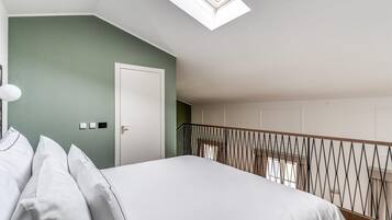 Un dormitorio con tragaluz, una cama con ropa de cama blanca, una puerta y una barandilla.