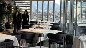 A modern restaurant with large windows offering a city view. Tables are set with white tablecloths and wine glasses. - Palazzo San Gottardo Lake Como, a Radisson Collection (Como)