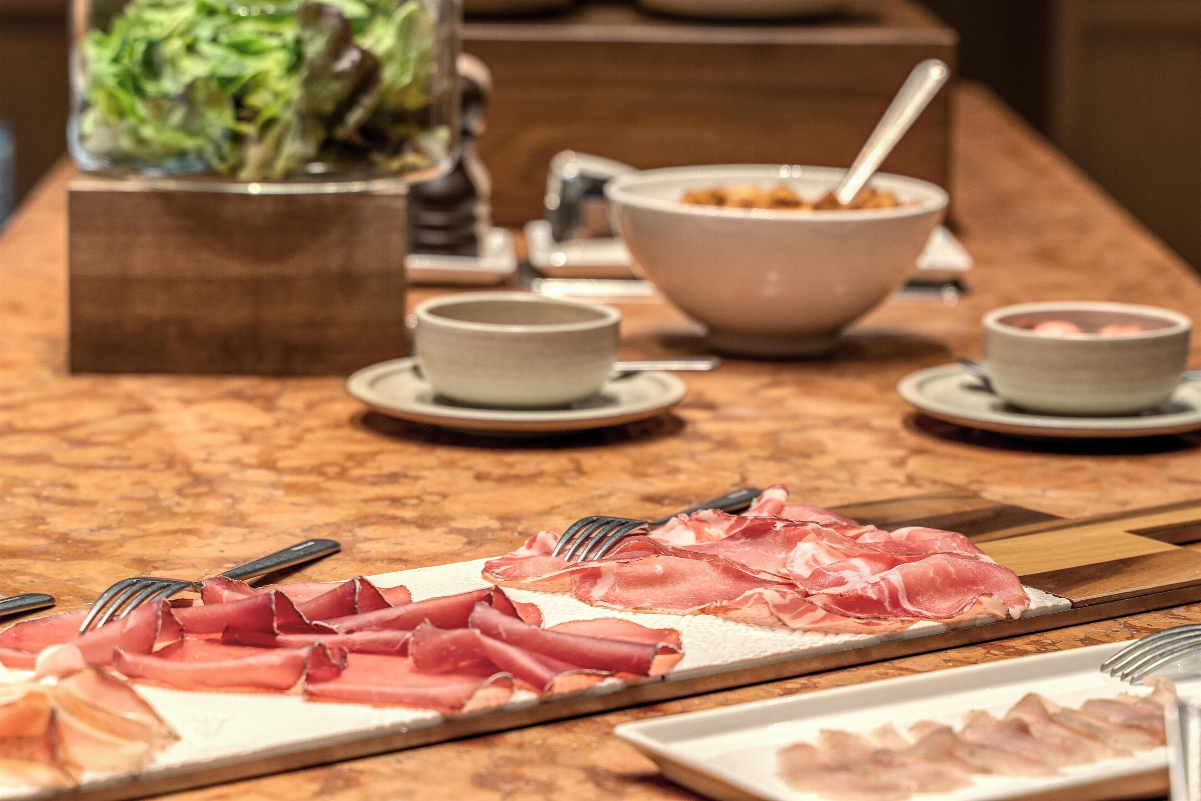 Una mesa de buffet con diversos alimentos, incluyendo carnes cortadas y tazones de sopa.