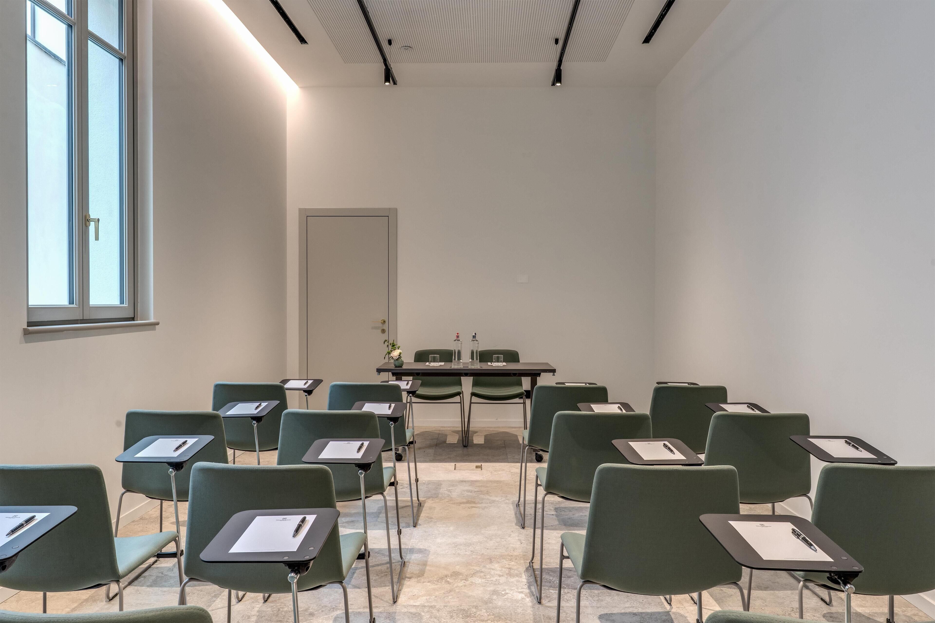 Ein Konferenzraum mit grünen Stühlen und Tischen, einem großen Fenster und einer Decke mit eingelassenen Leuchten.