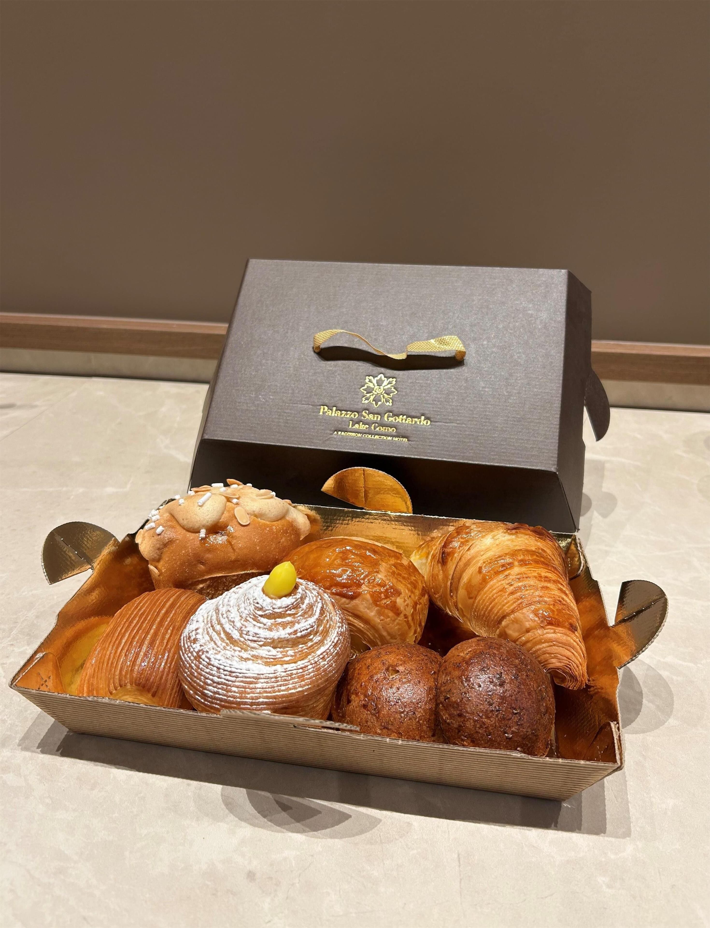 A box of assorted pastries including croissants, a cake, and a pastry with powdered sugar.