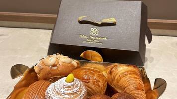 A box of assorted pastries including croissants, a cake, and a pastry with powdered sugar.