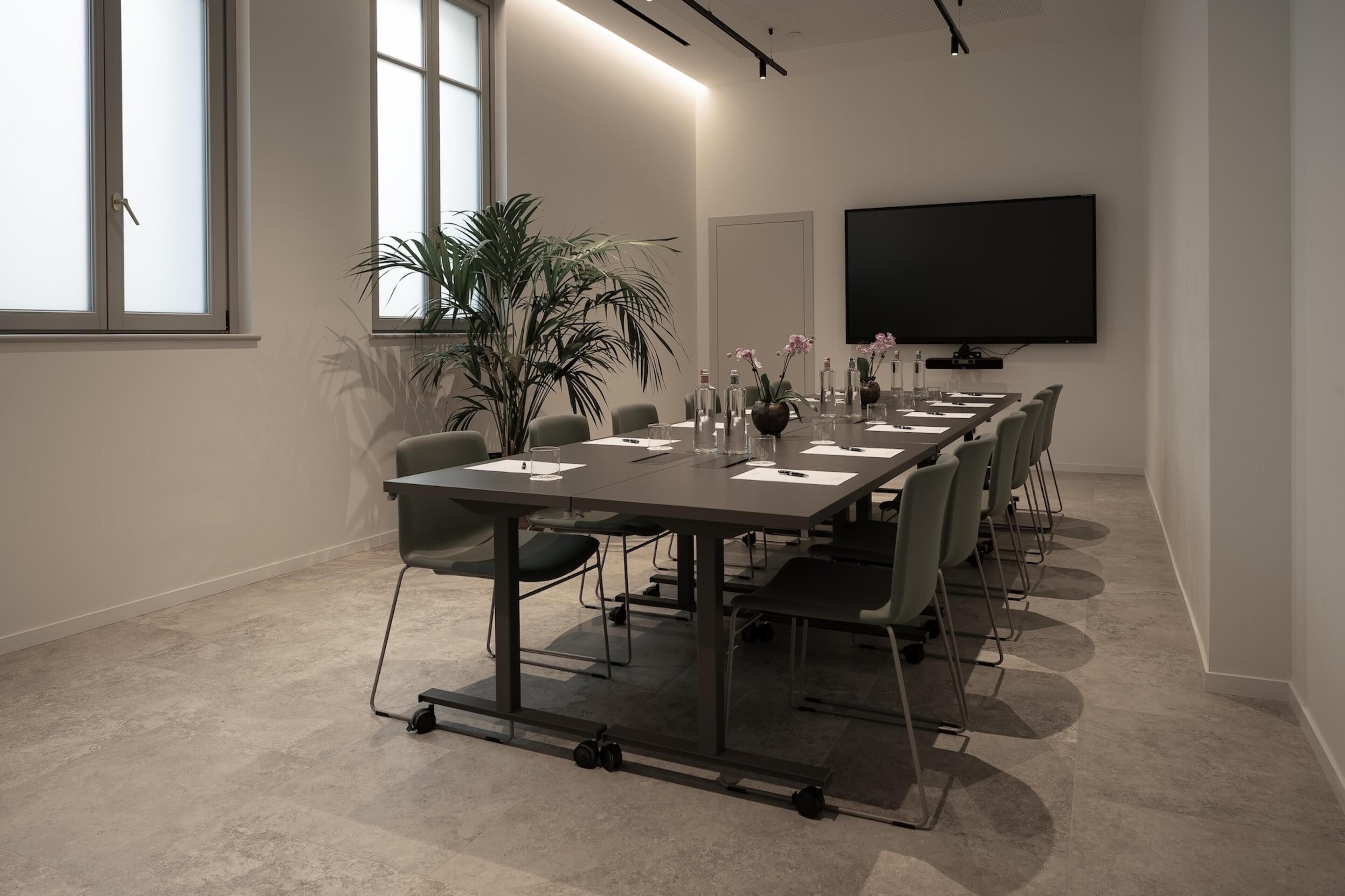 A conference room with a long table, chairs, a large screen, and potted plants.