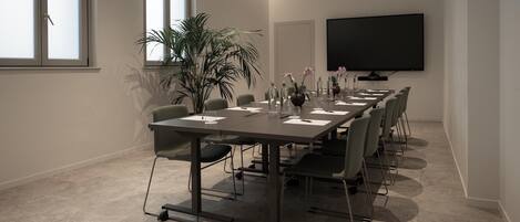 A conference room with a long table, chairs, a large screen, and potted plants.