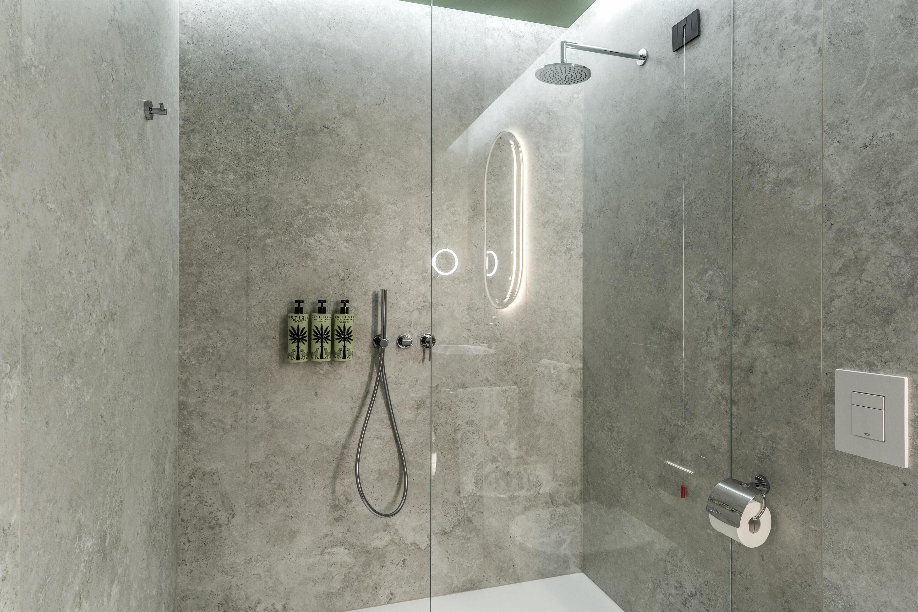 Une douche moderne dotée d’une porte en verre, d’un pommeau de douche à main et d’un porte-rouleau de papier toilette.