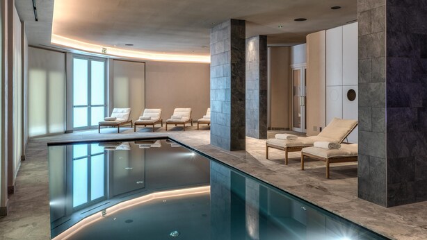 A modern indoor pool area with a glass barrier, lounge chairs, and a stone column. - Palazzo San Gottardo Lake Como, a Radisson Collection (Como)