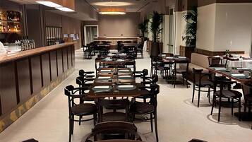 Un amplio vestíbulo de hotel con varias mesas y sillas para comer, una zona de bar y una gran lámpara circular en el techo.