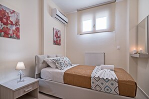 Une chambre à coucher comprenant un lit, une table de chevet, une lampe, un appareil de climatisation, une fenêtre et une œuvre d’art accrochée au mur.