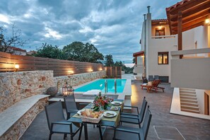 Un espace de restauration situé au bord de la piscine, avec des sièges en plein air, un mur en pierre et un bâtiment moderne en arrière-plan.