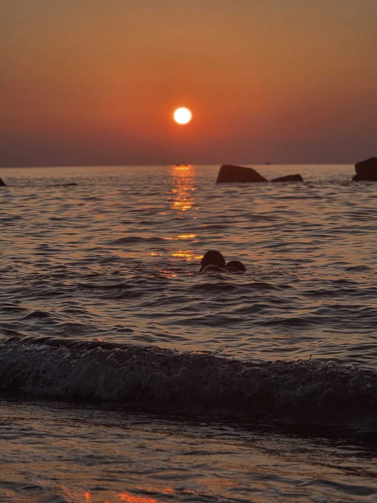 A sunset over the ocean with rocks in the water.