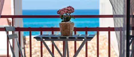 Un balcón con una maceta de mimbre que contiene flores rosadas, con vista a una playa.