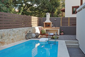 A swimming pool with a stone wall, a wooden deck, and a brick oven. - All Season Sun Villa (Rethymno)