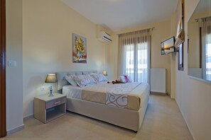 A bedroom with a bed, nightstand, lamp, air conditioning unit, and a painting on the wall. - All Season Sun Villa (Rethymno)