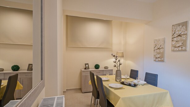 A dining area with a table set for two, a cabinet with decorative items, and wall-mounted artwork. - All Season Sun Villa (Rethymno)