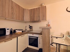A compact kitchen with wooden cabinets, a Bosch oven, a microwave, and a small bar stool. - Renovated studio in Courchevel 1850, ski-in/ski-out, 4 pax, parking included (Courchevel)