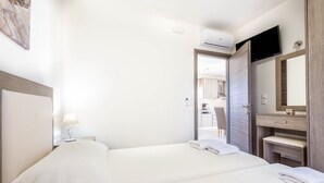 Une chambre d’hôtel avec deux lits, une table de chevet avec une lampe, un téléviseur fixé au-dessus du lit, une commode en bois avec un miroir et une porte donnant sur une salle de bain.