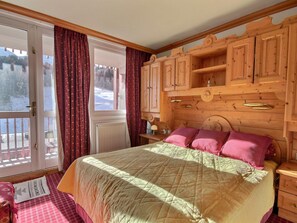 A cozy bedroom with a large bed, wooden headboard, and a view of a snowy landscape through the window. - Spacious apartment for 8 people with balcony facing the slopes (La Plagne)