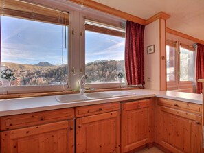 A kitchen with wooden cabinets, a white countertop, a sink, and a window with a view of a mountainous landscape. - Spacious apartment for 8 people with balcony facing the slopes (La Plagne)