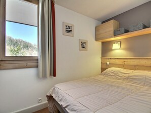 Ein Schlafzimmer mit einem Bett, einem Fenster mit Blick auf Bäume, einem Kopfteil und zwei gerahmten Bildern an der Wand.