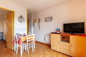 Een eethoek met een tafel en stoelen, een televisie op een dressoir en een kast met lades.
